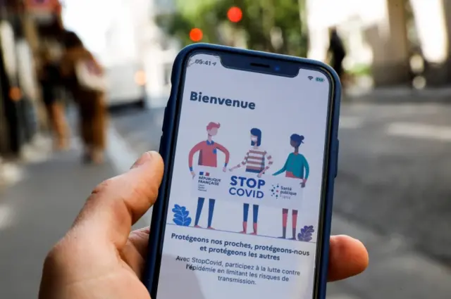 A person holding up a phone showing the StopCovid app