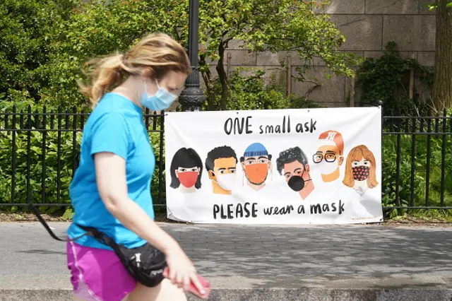 A person wearing protective face mask walks by a sign that reads "One small ask, please wear a mask"