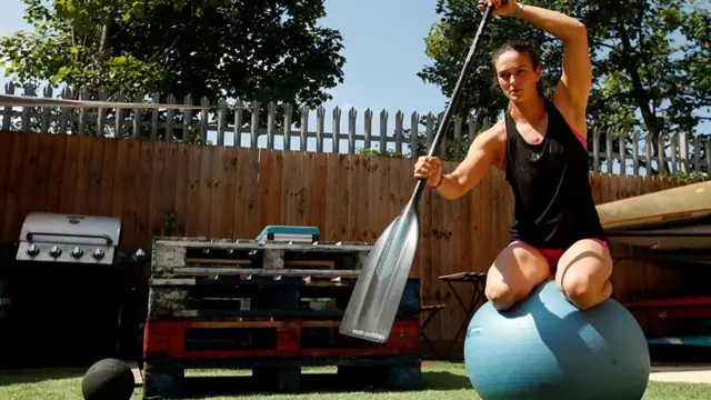 An athlete balances on a pilates ball while practising with a canoe paddle