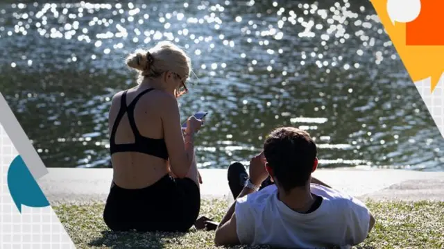 A woman and a man sit next to a lake in the sunshine