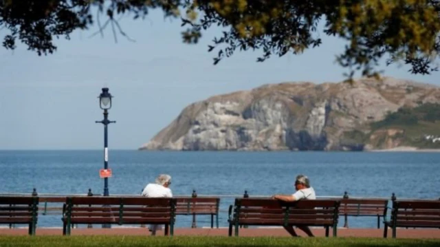 Two people sit on benches in Llandudno, Conwy