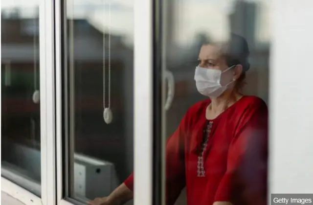 A woman wearing a face mask at a window