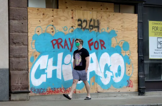 A man wearing a mask walks past graffiti saying "pray for Chicago"