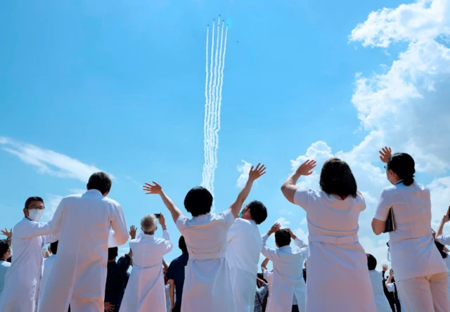 Medical workers react as they watch the Blue Impulse aerobatics team of the Japan Air Self-Defense Force perform over Tokyo