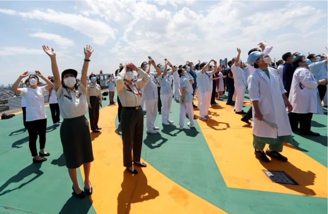 Medical workers react as they watch the Blue Impulse aerobatics team of the Japan Air Self-Defense Force perform over Tokyo