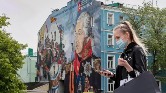 A woman wearing a protective mask walks in front of a mural of the Russian military commander Mikhail Kutuzov in Moscow