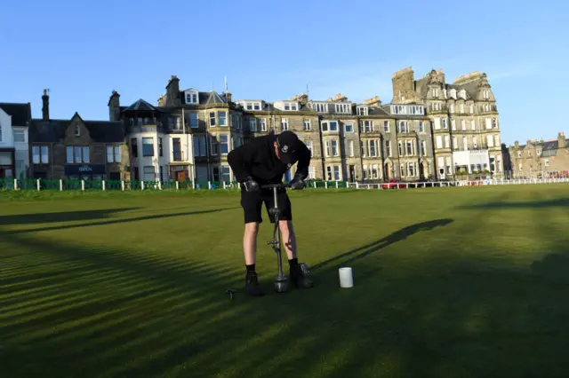 A member of the grounds staff cuts a hole on the green