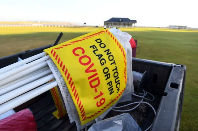 A social distancing sign is transported across the green at The Old Course