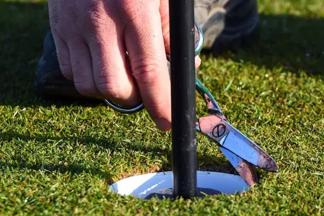 A member of the grounds staff cuts a hole on the green