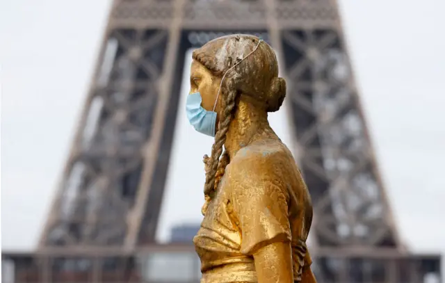 A golden statue at the Trocadero square near the Eiffel Tower wears a protective face mask