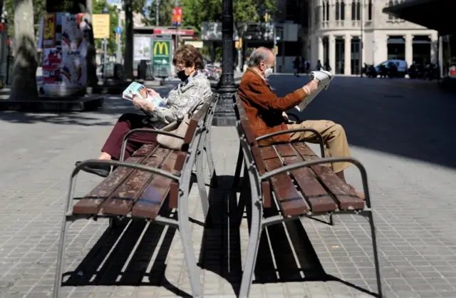Two people wearing face masks sit on a bench in Barcelona