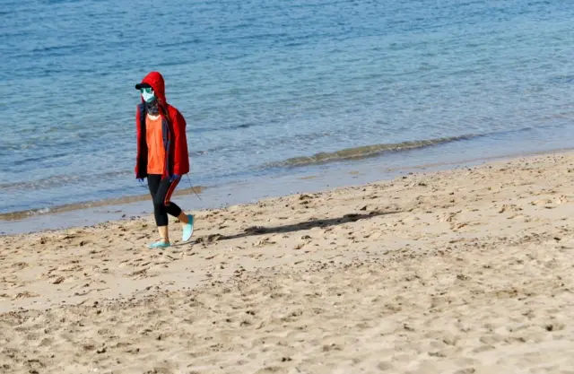 A woman wearing a face mask walks along a beach on the island of Lanzarote