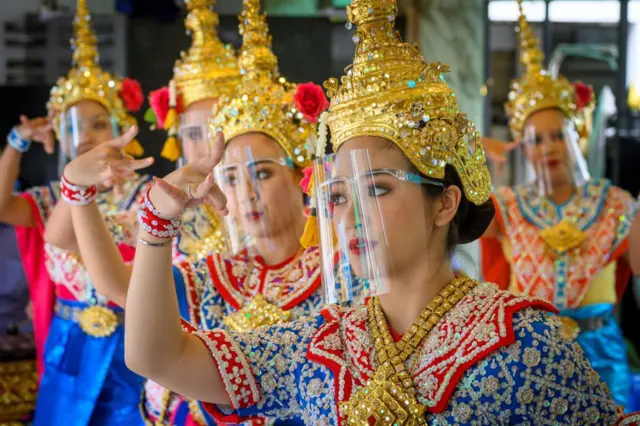Traditional Thai dancers wearing protective face shields perform at the Erawan Shrine