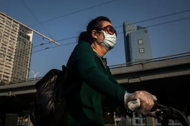 A woman wears a mask while riding a bicycle past the gate of Zhongshan Park on April 28, 2020 in Wuhan, China.