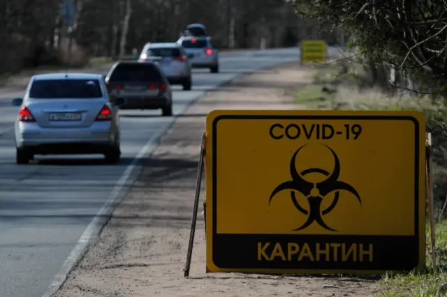 Cars drive past a sign reading "COVID-19 Quarantine" on a road towards Pervomayskoye settlement