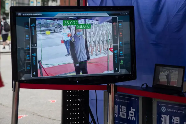 A display screen of a temperature-monitoring camera shows a student entering a high school in Wuhan