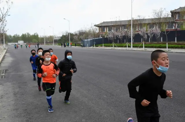 his picture taken on April 9, 2020 shows a group of children wearing face masks, amid concerns of the COVID-19 coronavirus, running along a street in Beijing.