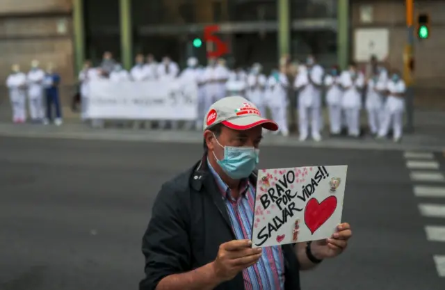 A man holds a sign that reads: "Bravo for saving lives" in front of health workers