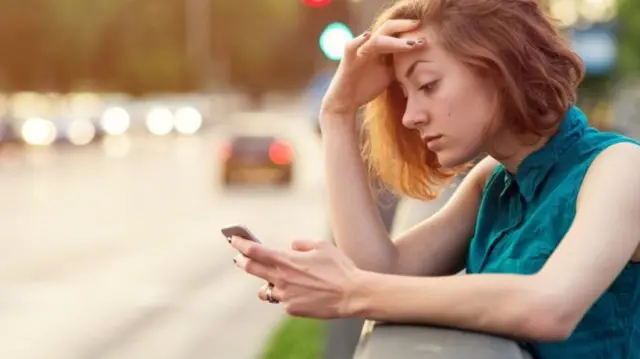 A young woman looks at her phone by a road