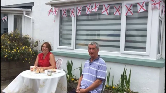 Man and woman sit beside each other at table in front garden