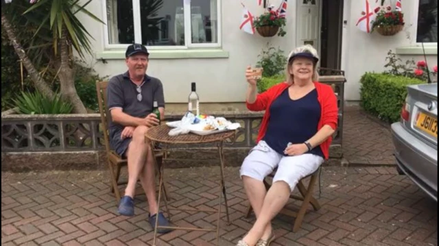 Man and woman sit at a table on their drive with glasses in hand