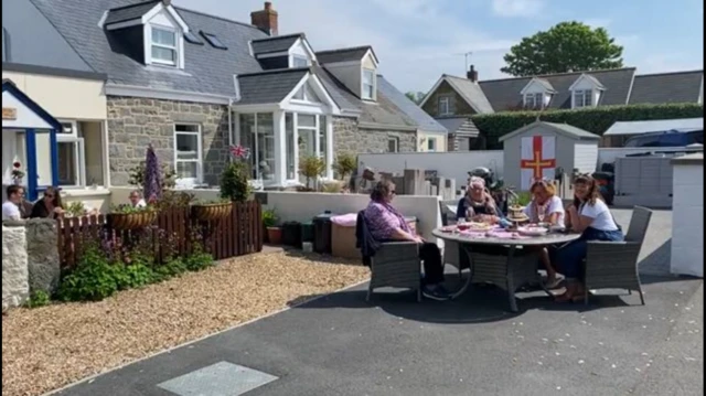 Family sit around table in front garden