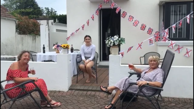 Three women sitting outside home with Liberation flags