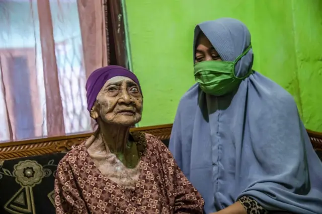 Kamtim, 100, sits in her living room with her daughter-in-law Siti Aminah (R) in Surabaya on 31 May after being discharged from a hospital.