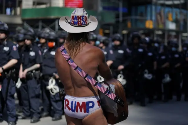 The famous Times Square performer known as the Naked Cowboy stands beside a police cordon