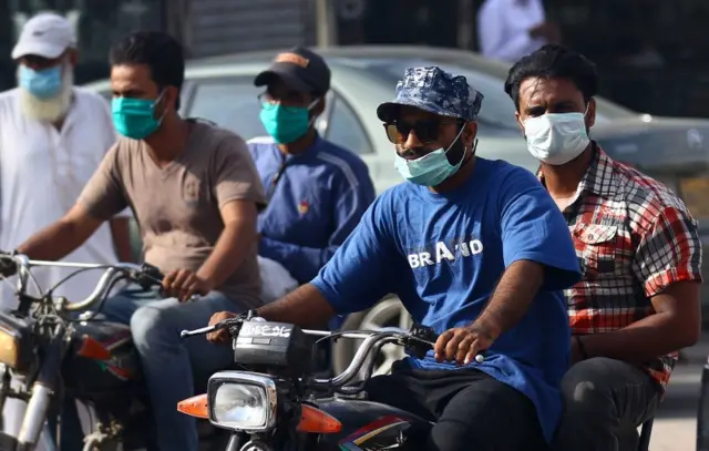 People wear masks as they ride motorbikes in Karachi