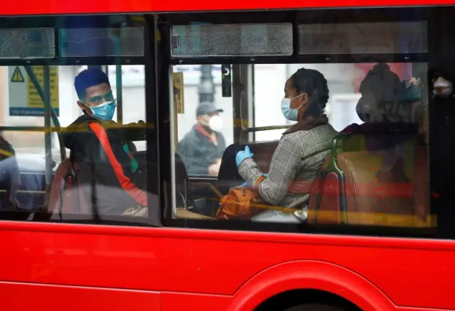 People wearing masks sit on a London bus