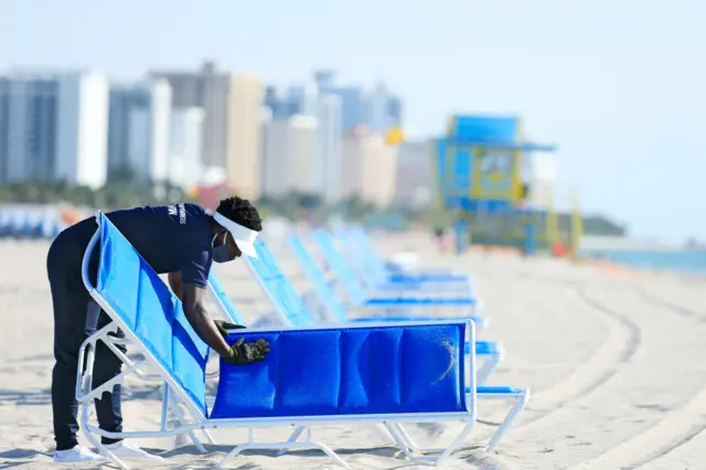 A man sets up rental beach lounge chairs on South Beach, June 10, 2020 in Miami Beach, Florida