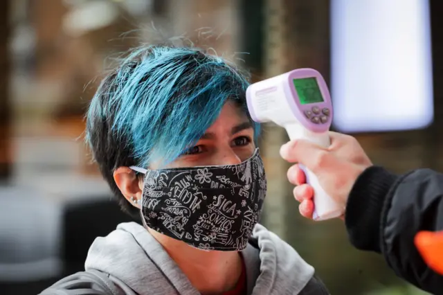 A worker takes the temperature of a woman before she enters a mall in Montevideo, Uruguay, 09 June 2020