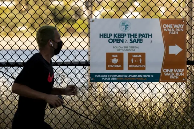 A jogger in Los Angeles runs past a sign showing social-distancing guidelines for a walk/run path