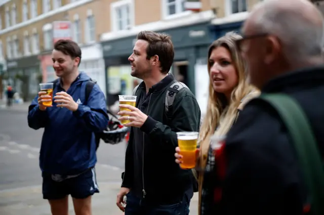 Customers drink takeaway beer outside a pub in Broadway Market, London