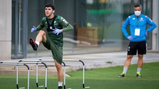 Real Betis midfielder Carles Alena wearing gloves as he trains during the coronavirus lockdown, watched by a coach wearing a face mask