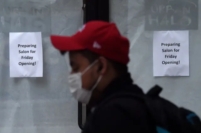 A man, wearing a face mask, walks past a hair salon ready to reopen in Arlington, Virginia