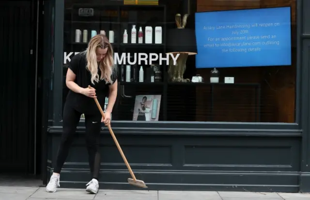 A hair salon worker in Dublin sweeps outside her premises