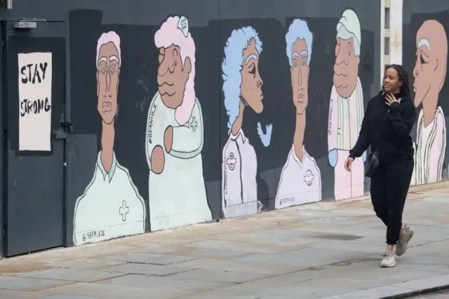 A woman passes a mural showing BAME medical, transport and construction workers, in London,