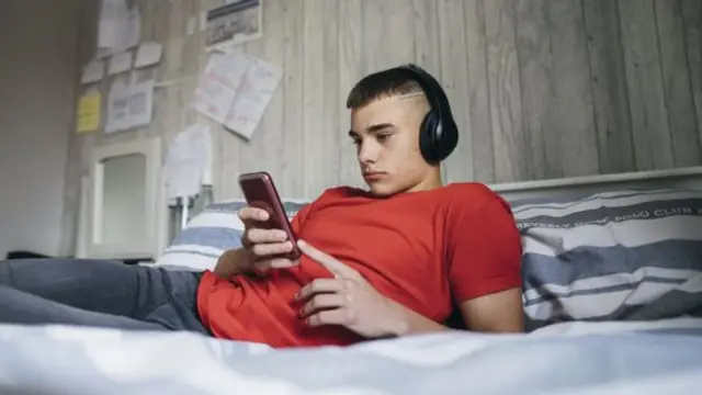 A young man wearing headphones on a bed