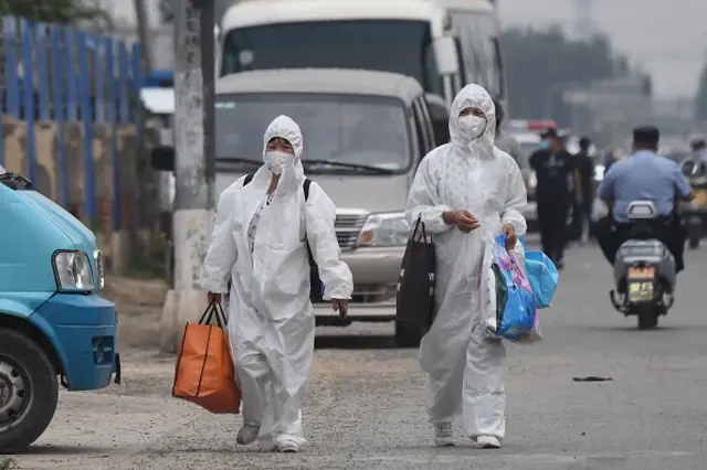 Two women wear protective suits as they walk on a street near the closed Xinfadi market in Beijing