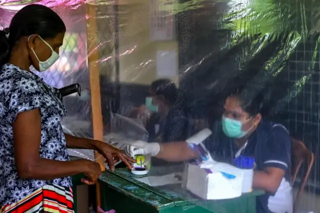 An election official behind a plastic sheet marks the finger of a voter (L) with ink during a mock election to test the guidelines implemented against the COVID-19 coronavirus in Ingiriya of Kalutara District in Western Province on June 14, 2020.