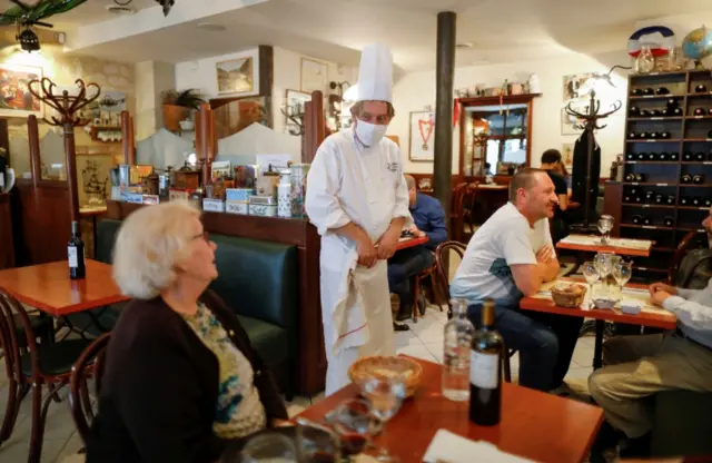 A chef wearing a protective face mask talks to customers