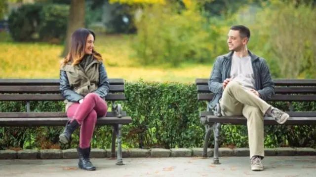 Two people sit apart on two benches