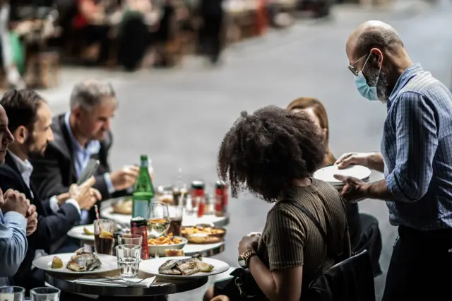 A waiter serves customers at a terrace of a restaurant in Paris, on 15 June