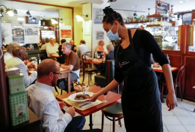 An employee, wearing a protective face mask, serves customers in Paris on Monday