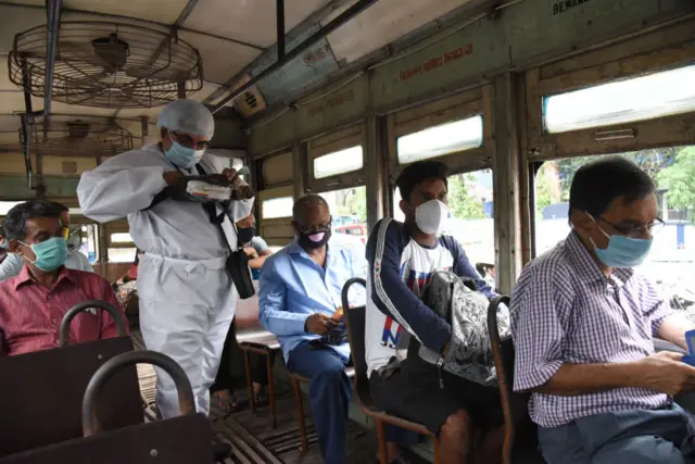 A tram conductor wearing a protective suit while collecting tickets from passengers after the authorities permitted to resume its services