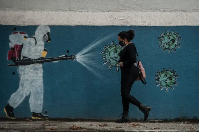 A woman wearing a protective mask is seen walking in front of graffiti in central Rio de Janeiro