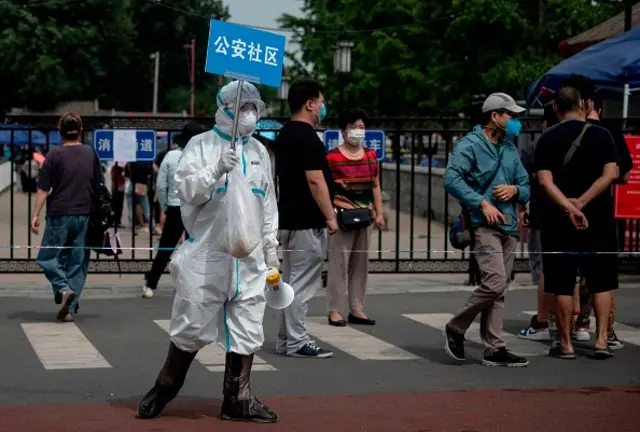 A member of the medical staff in full protective gear holds up a sign to assist people near the market believed to be the source