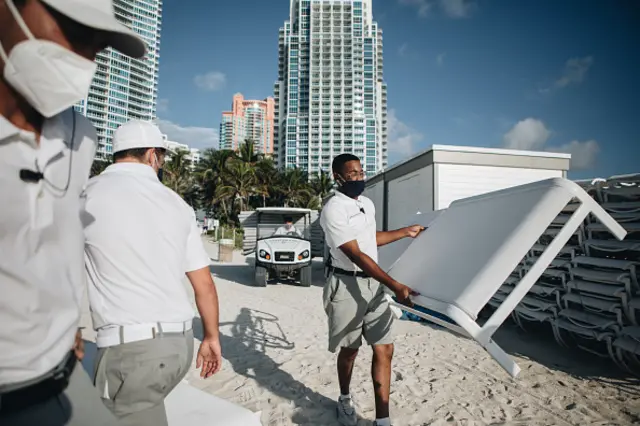 An employee wearing a protective mask sets up beach chairs for customers in Miami Beach, Florida